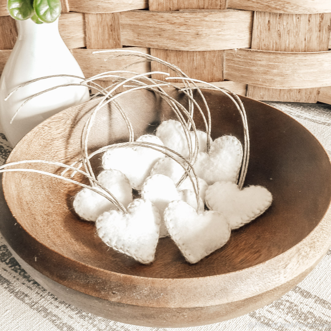 A wooden bowl filled with white felt heart ornaments
